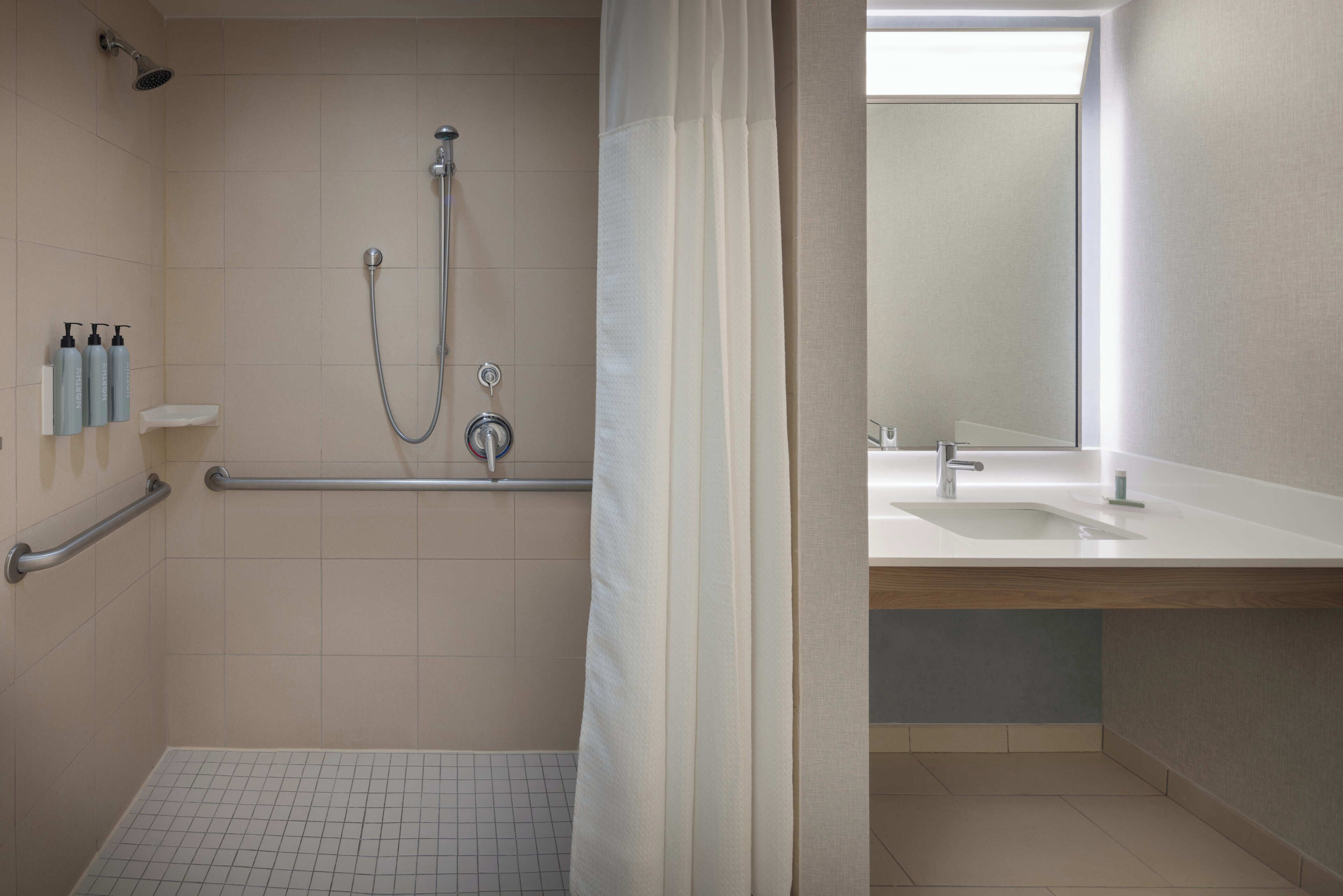 A bathroom with a shower, grab bars, a sink, and a mirror.