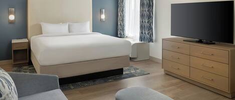 A modern hotel room with a large bed, a flat-screen TV, a wooden dresser, and a seating area.