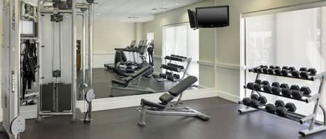 Un gimnasio con máquinas de cardio, equipo de levantamiento de pesas y una televisión montada en la pared.