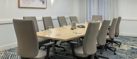 A conference room with a rectangular table, eight chairs, and a carpeted floor.