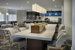Una hall d'albergo moderna con un'isola centrale, diverse zone relax e un'area cucina visibile.