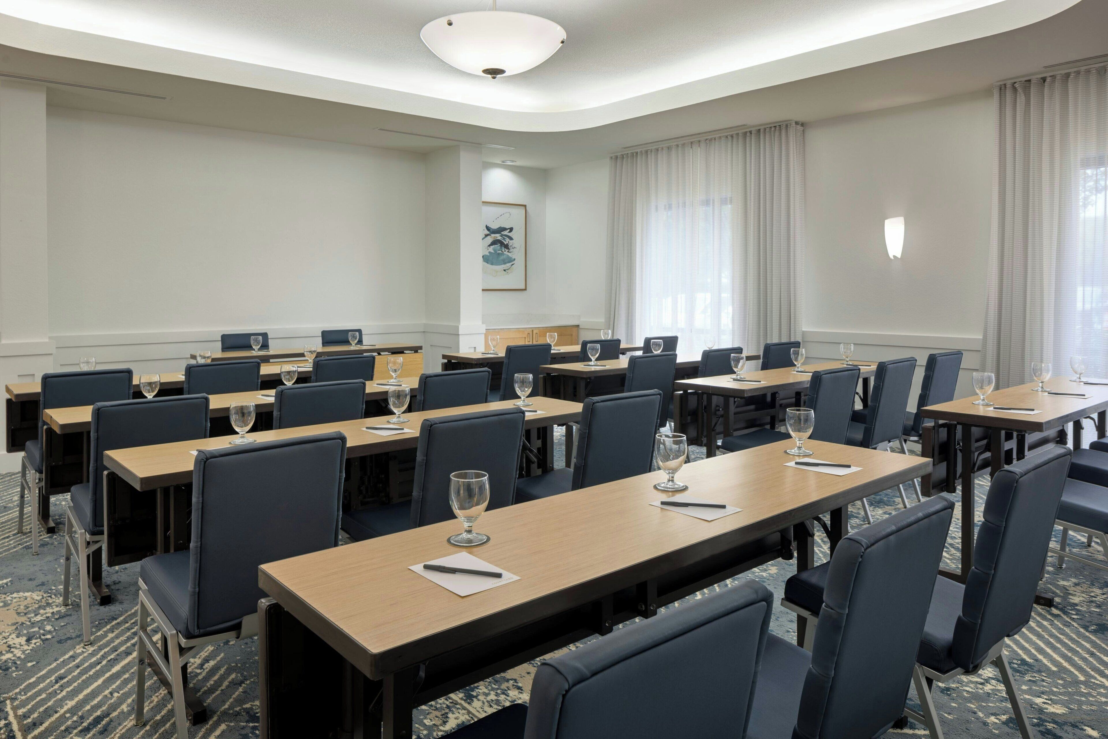 Une salle de conférence équipée de plusieurs tables et de chaises, chacune agrémentée d’un verre à vin et d’un bloc-notes.