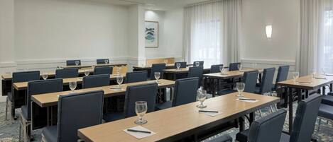 A conference room with multiple tables and chairs, each with a wine glass and notepad.
