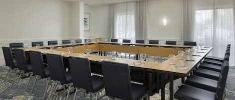 Une salle de conférence avec une longue table, des chaises noires et un sol recouvert de moquette.