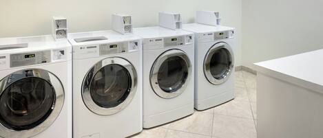 Varias lavadoras de carga frontal blancas en un cuarto de lavado con piso de baldosas.