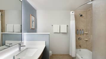 Une salle de bain moderne avec un grand miroir, un lavabo, une douche et une baignoire. Des serviettes sont accrochées au mur et des articles de toilette sont posés sur une étagère.