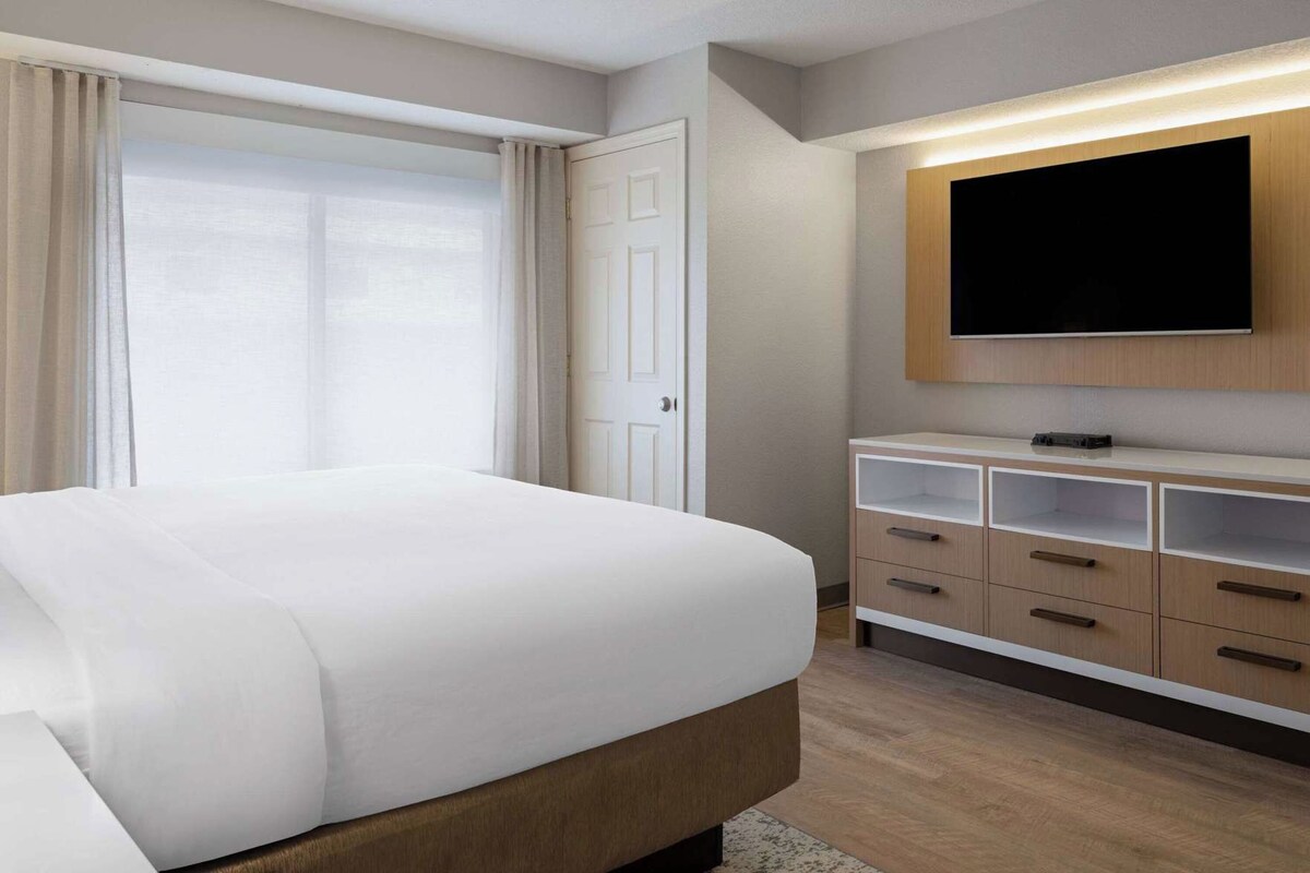 A hotel room with a bed, a TV mounted on the wall, and a wooden dresser.