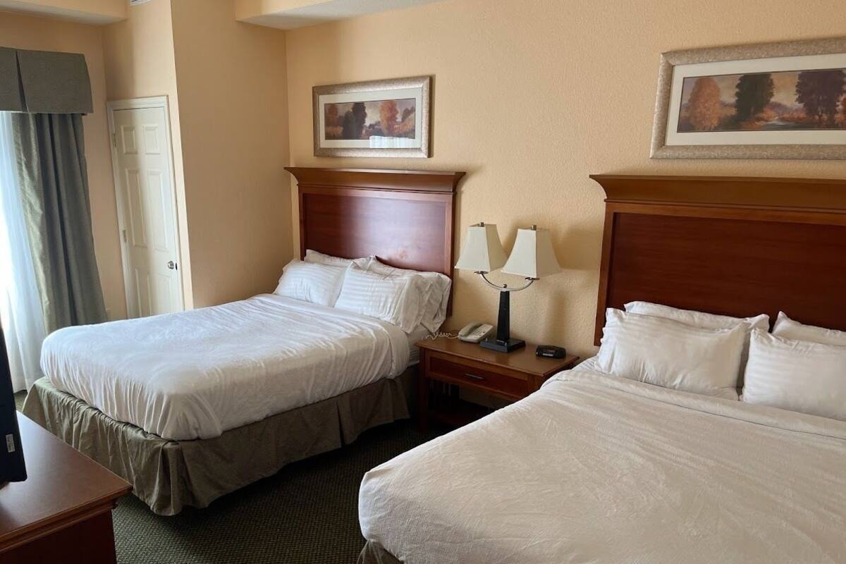 A hotel room with two beds, a desk, a telephone, and a painting on the wall.
