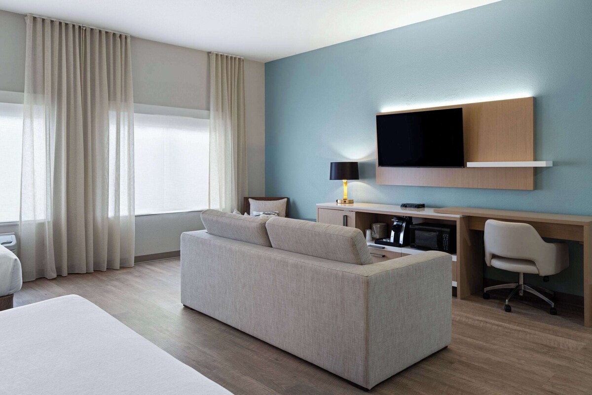 A modern hotel room with a sofa, a desk with a flat-screen TV, a lamp, and a microwave.
