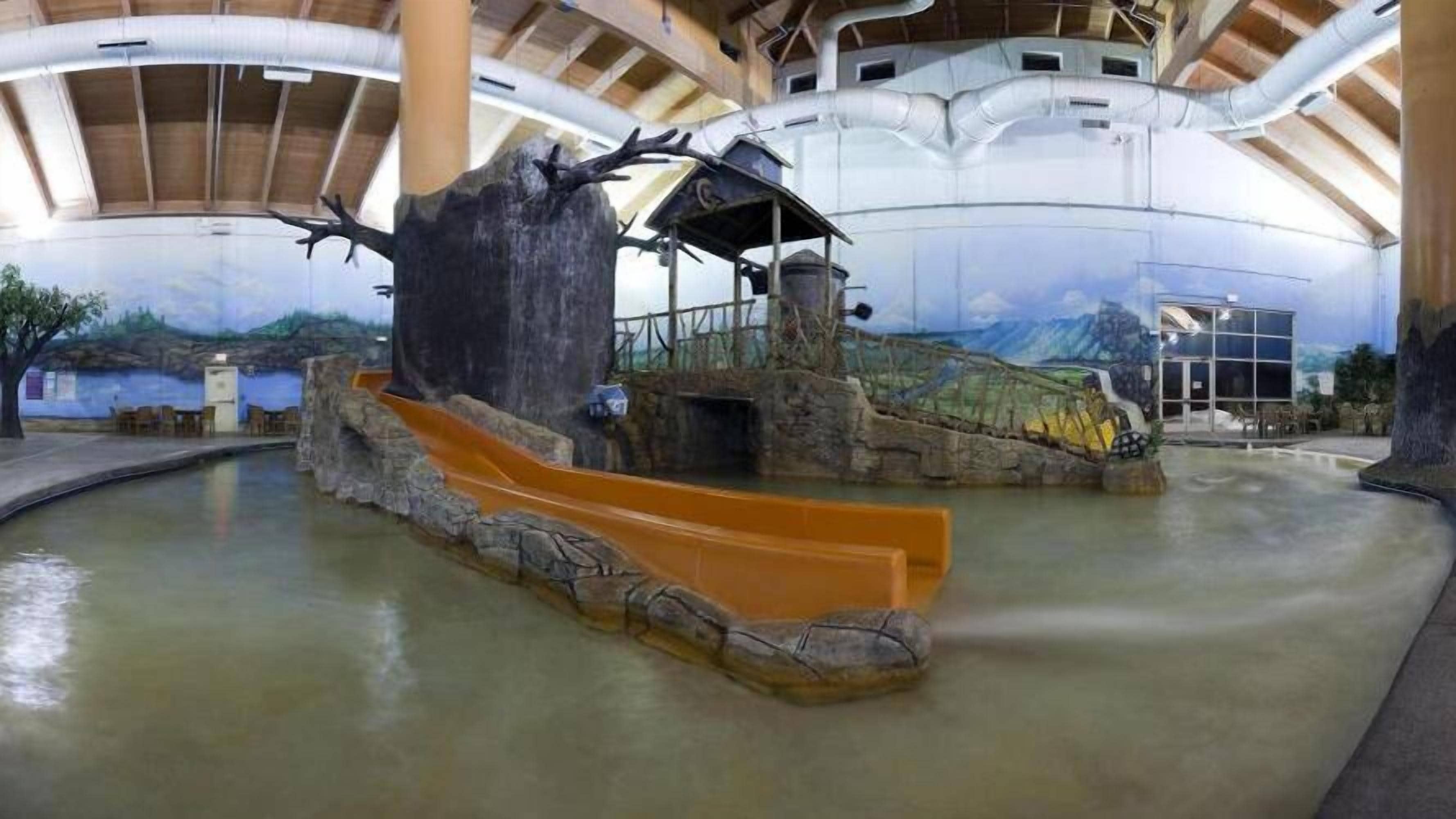 Un toboggan aquatique intérieur avec un décor de paysage rocheux, une structure en bois et une vue dégagée sur les environs.
