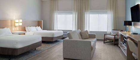 Quarto de hotel com duas camas, um sofá, uma escrivaninha e uma televisão.