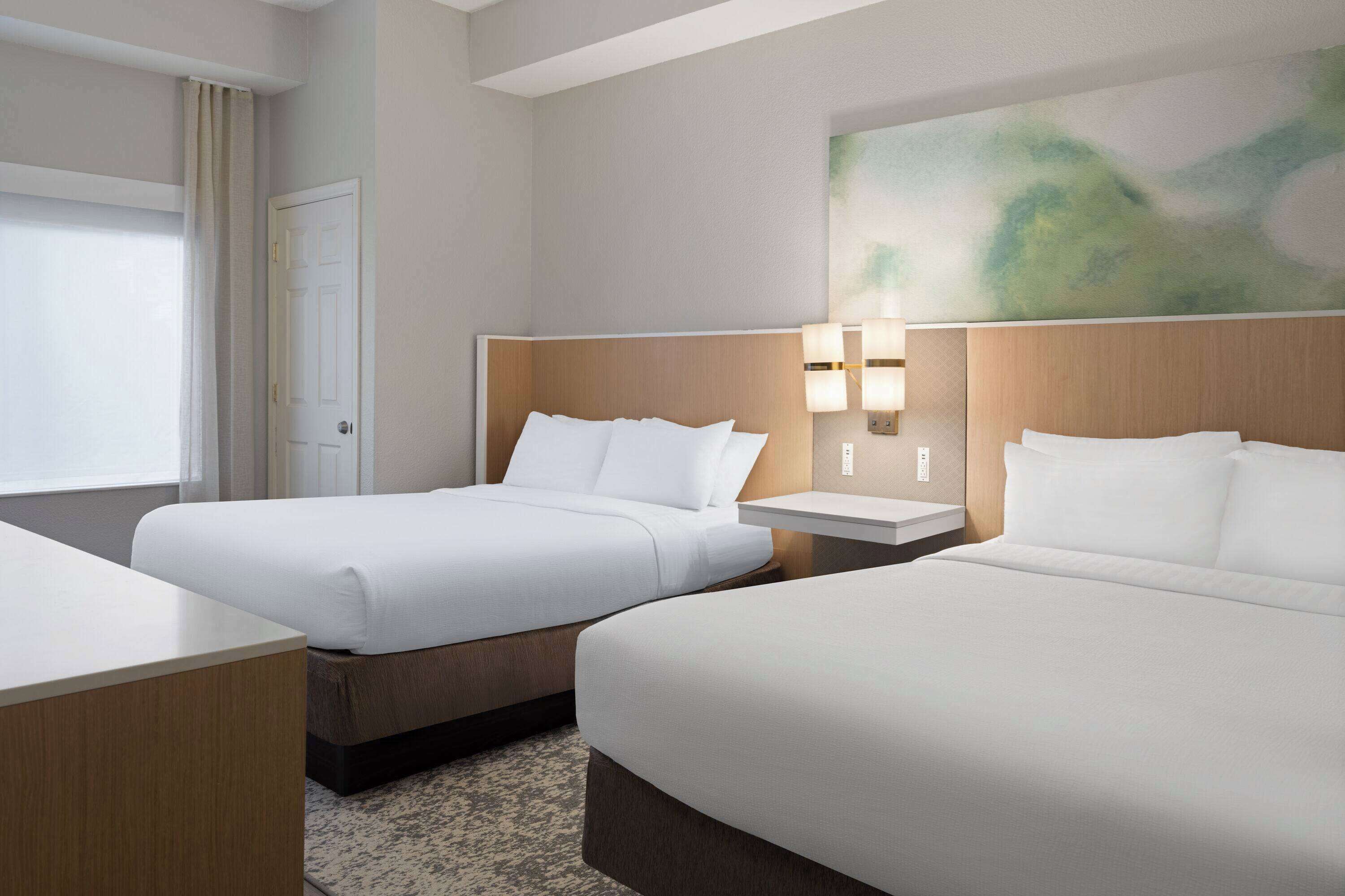 Une chambre d’hôtel avec deux lits, un bureau, une lampe et un tableau au mur.
