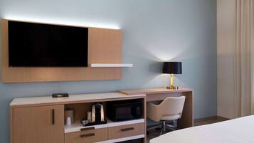 A hotel room with a bed, a desk with a lamp, a microwave, and a TV mounted on the wall.