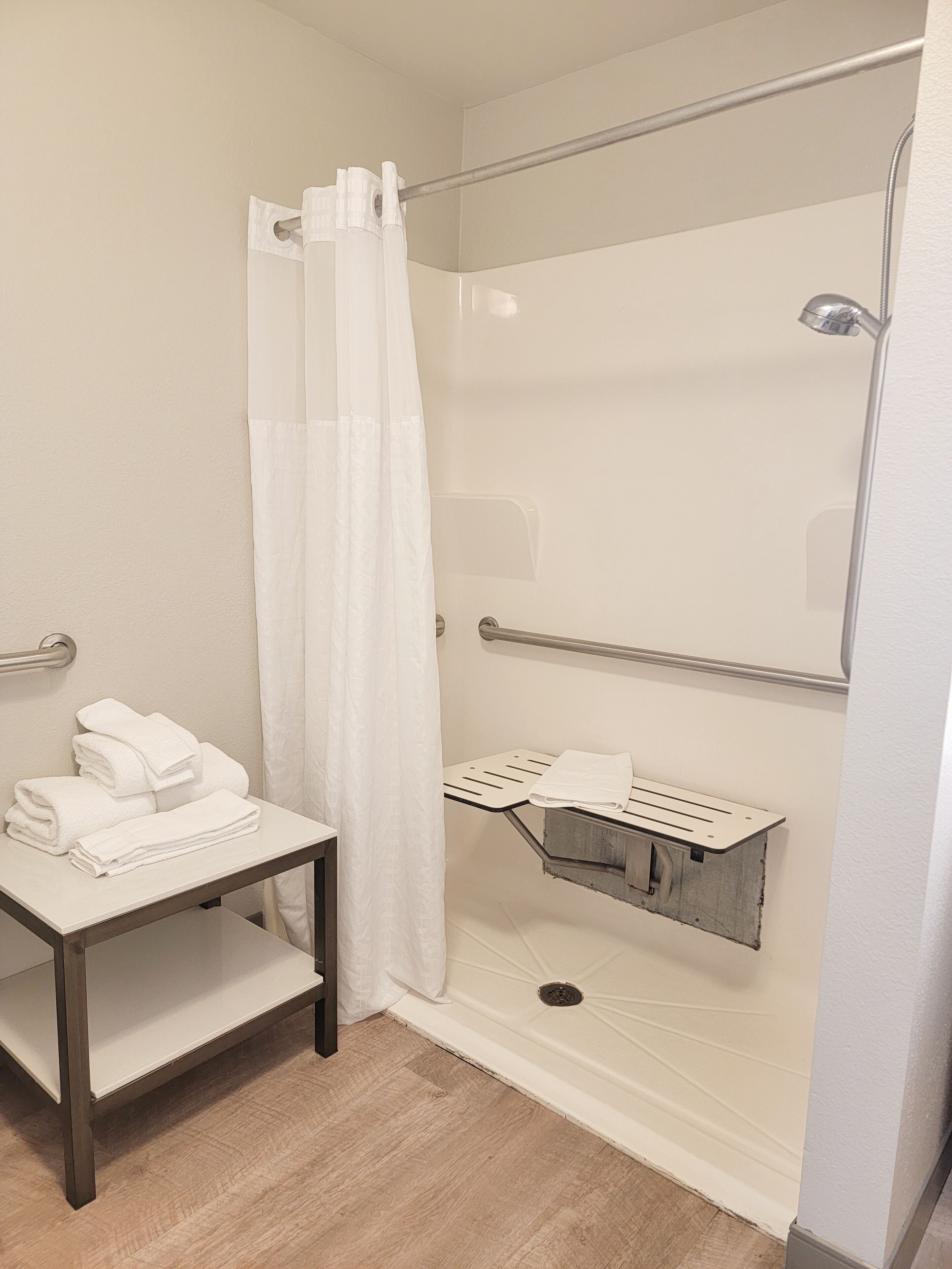 Un baño pequeño y moderno con ducha, toallero y repisa con toallas.