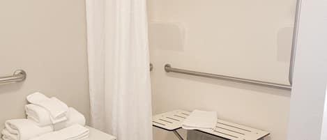 Un baño pequeño y moderno con ducha, toallero y repisa con toallas.