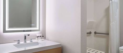 Un baño con un lavamanos blanco, un espejo con luz y una zona de ducha.