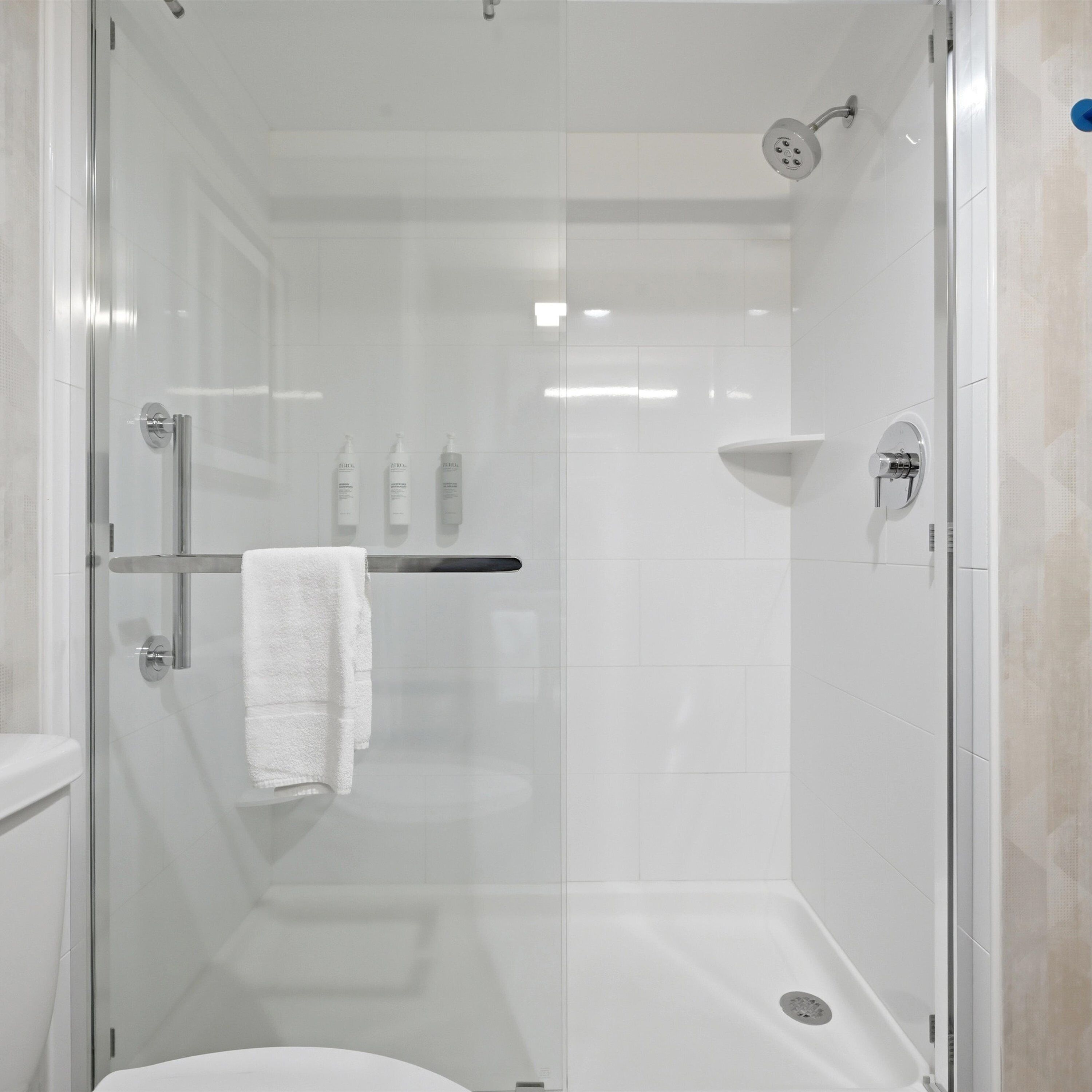 Een douche met glazen wanden, een witte handdoek aan een rek, een handdouche en een kraan op de muur.