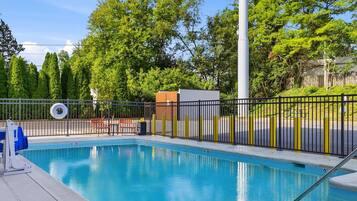 Una piscina con cercado metálico, un puesto de socorrista y una banca.