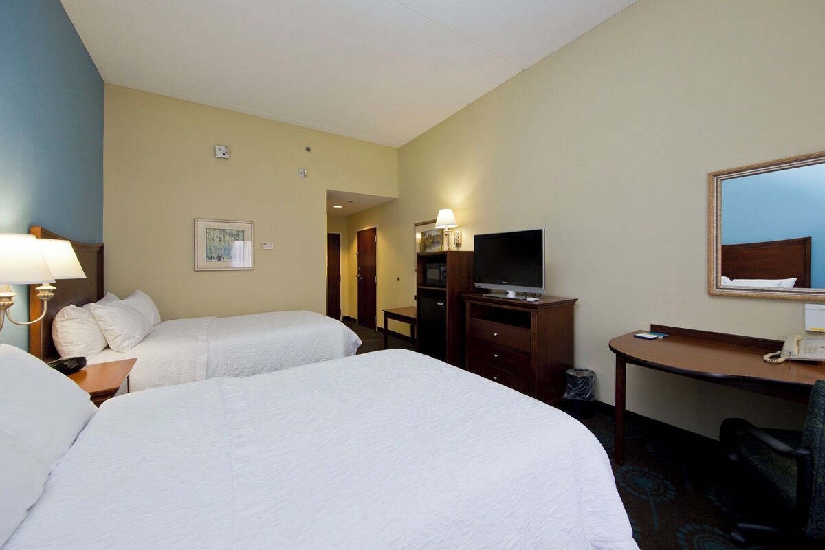 A hotel room with two beds, a desk with a telephone, a television, and a mirror.
