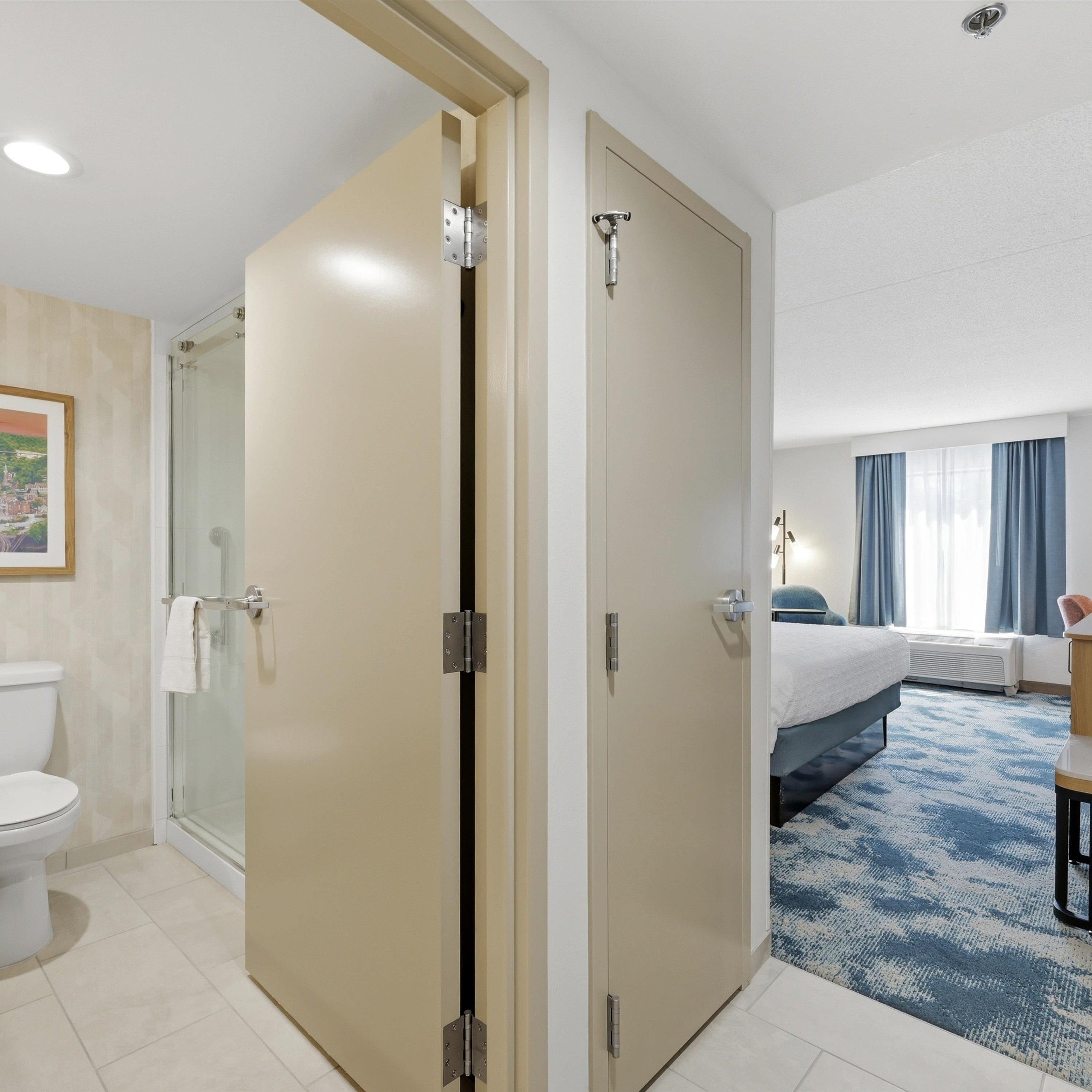 Habitació d'hotel amb dutxa, vàter, llit i una finestra gran amb cortines.