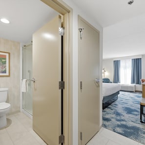 Quarto de hotel com chuveiro, vaso sanitário, cama e uma janela grande.