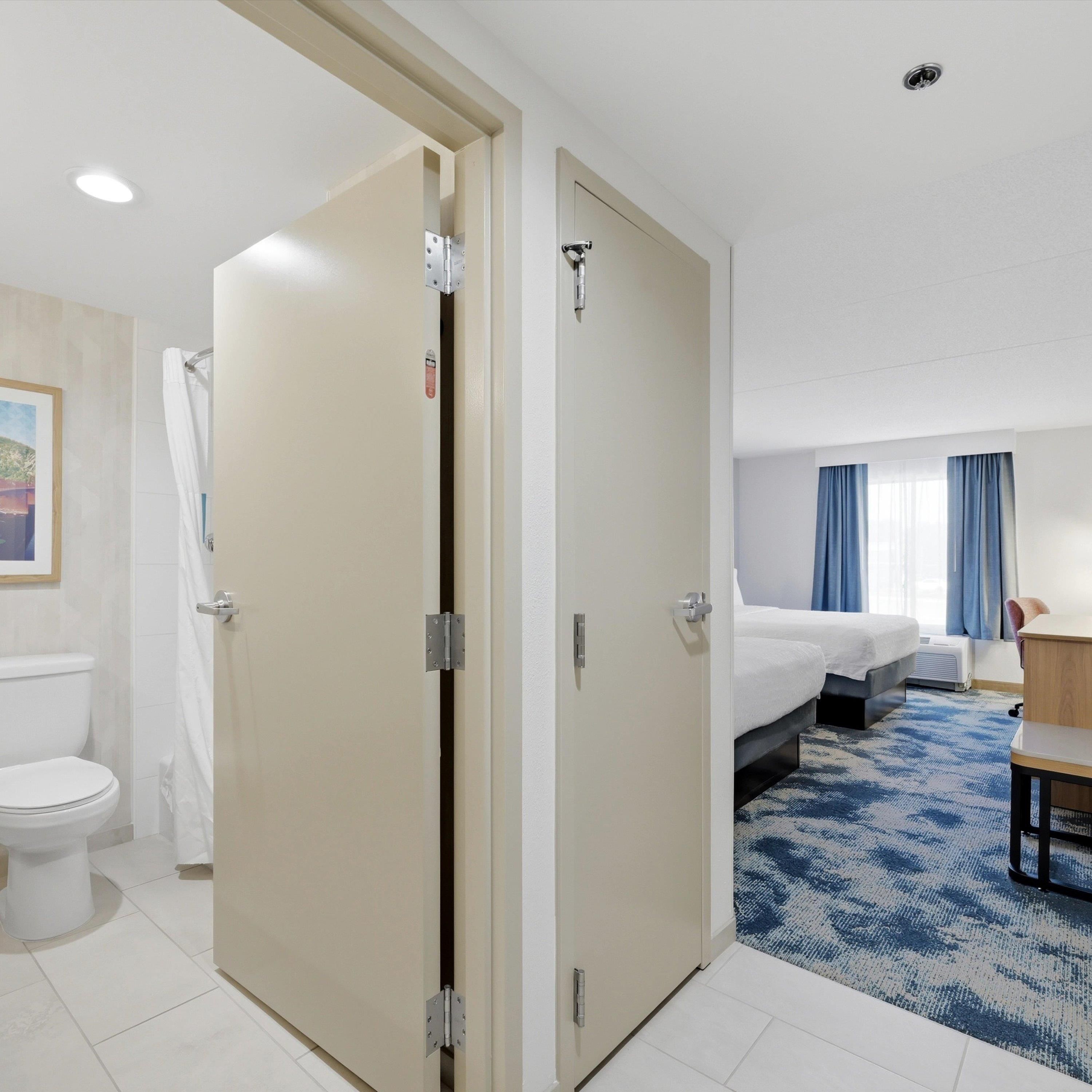 A hotel room with a bed, a desk, a chair, a toilet, and a shower area.