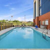A swimming pool with a metal fence, lounge chairs, and a building with a brick facade.
