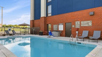 A swimming pool area with lounge chairs and a building with a sign reading 'Hampton by Hilton'.