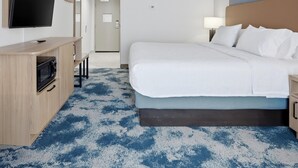 Una habitación de hotel con cama, televisión, escritorio con microondas y alfombra estampada.