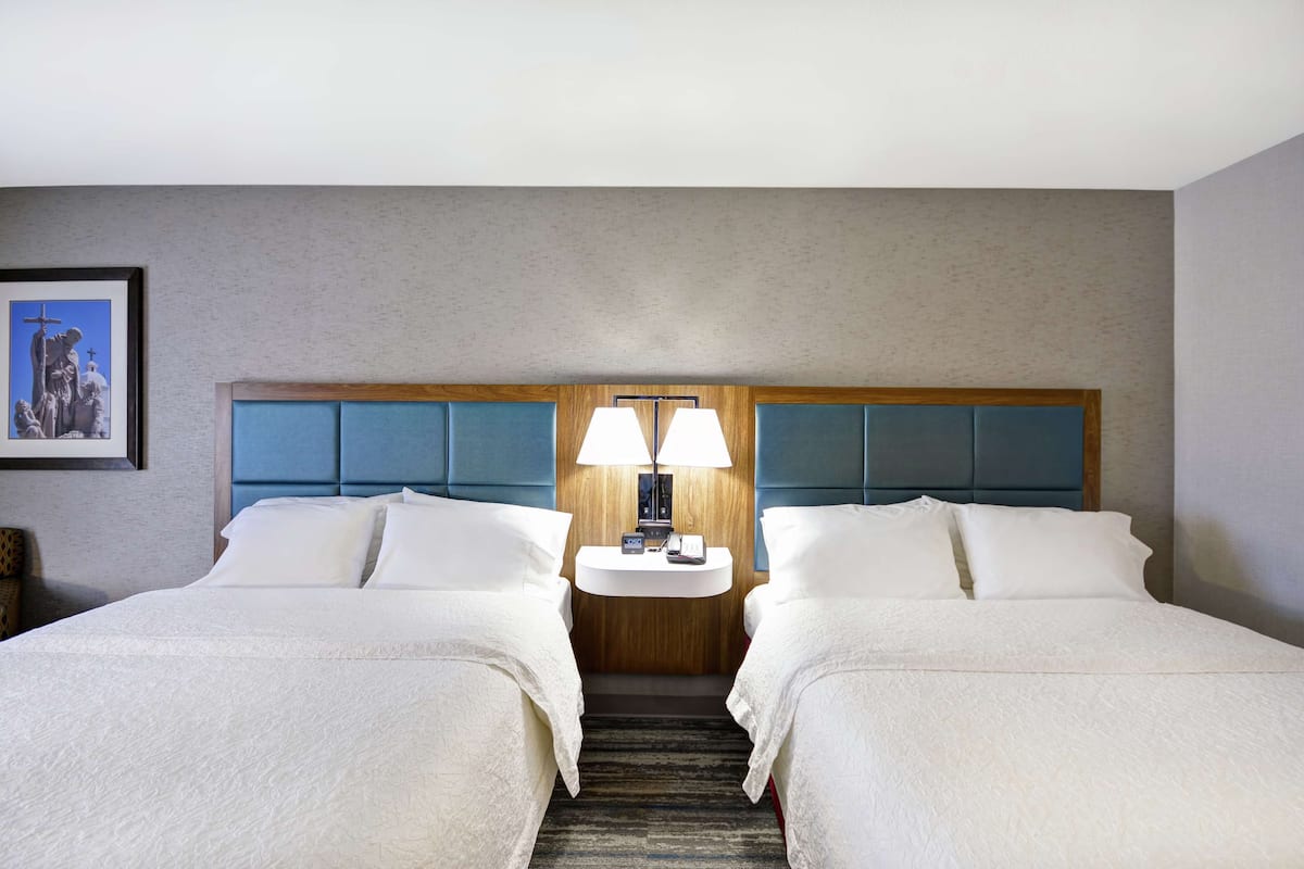 Ein Hotelzimmer mit zwei Betten, einem Nachttisch mit Lampe und einem gerahmten Bild an der Wand.