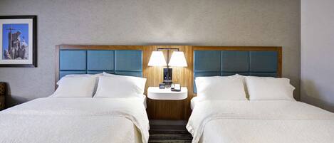 A hotel room with two beds, a nightstand with a lamp, and a framed picture on the wall.