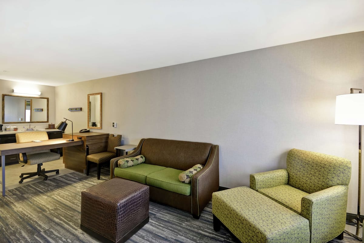 Ein Hotelzimmer mit Schreibtisch, zwei Sesseln, einem Sofa, einem kleinen Hocker und einer Lampe.
