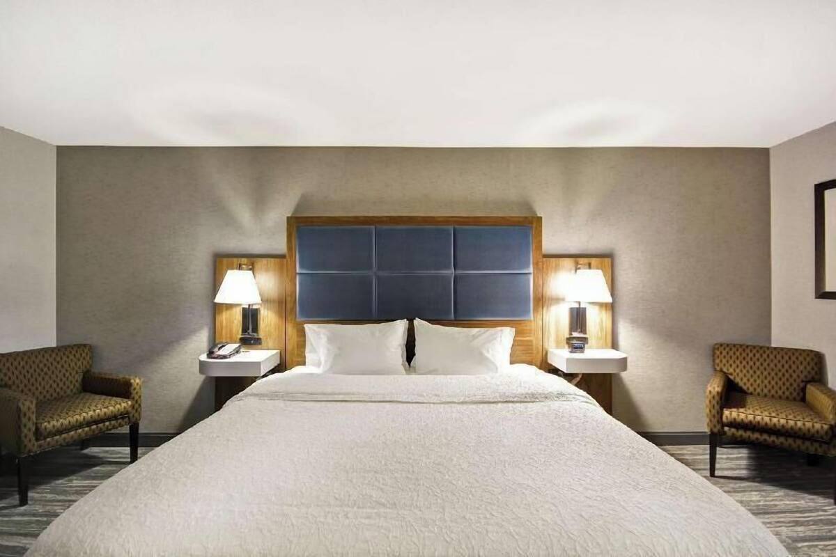 Ein Hotelzimmer mit einem großen Bett, zwei Nachttischen mit Lampen und zwei gemusterten Sesseln.