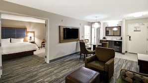 Habitación de hotel con cama, televisión, escritorio con sillas, zona de comedor y baño.
