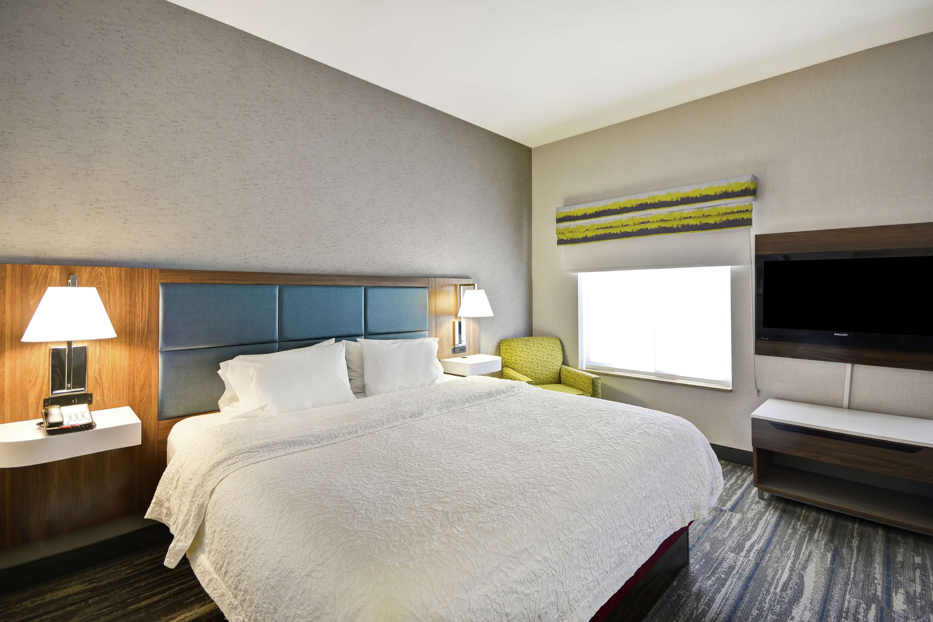Une chambre d’hôtel dotée d’un grand lit, d’un téléviseur à écran plat, d’un bureau avec une lampe, d’une chaise et d’une fenêtre donnant sur un paysage agréable.