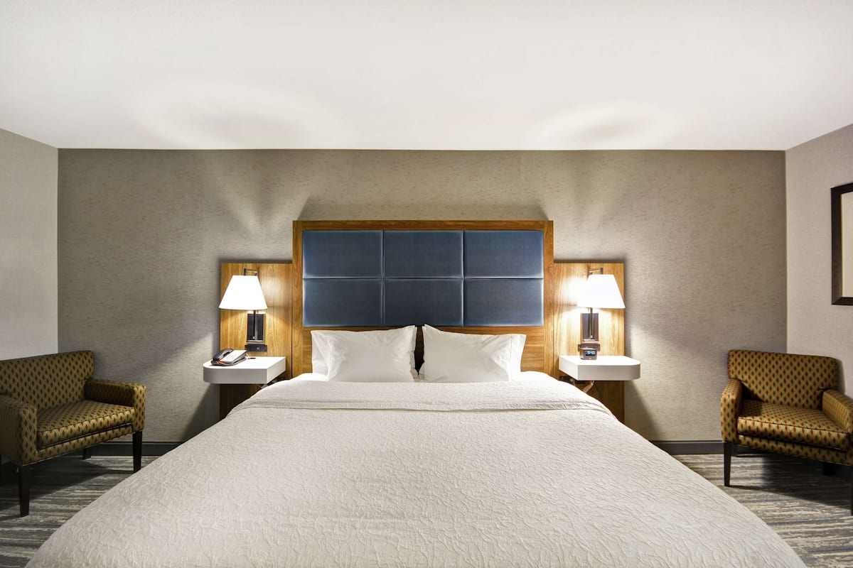 Ein Hotelzimmer mit einem großen Bett, zwei Nachttischen mit Lampen und zwei gemusterten Sesseln.