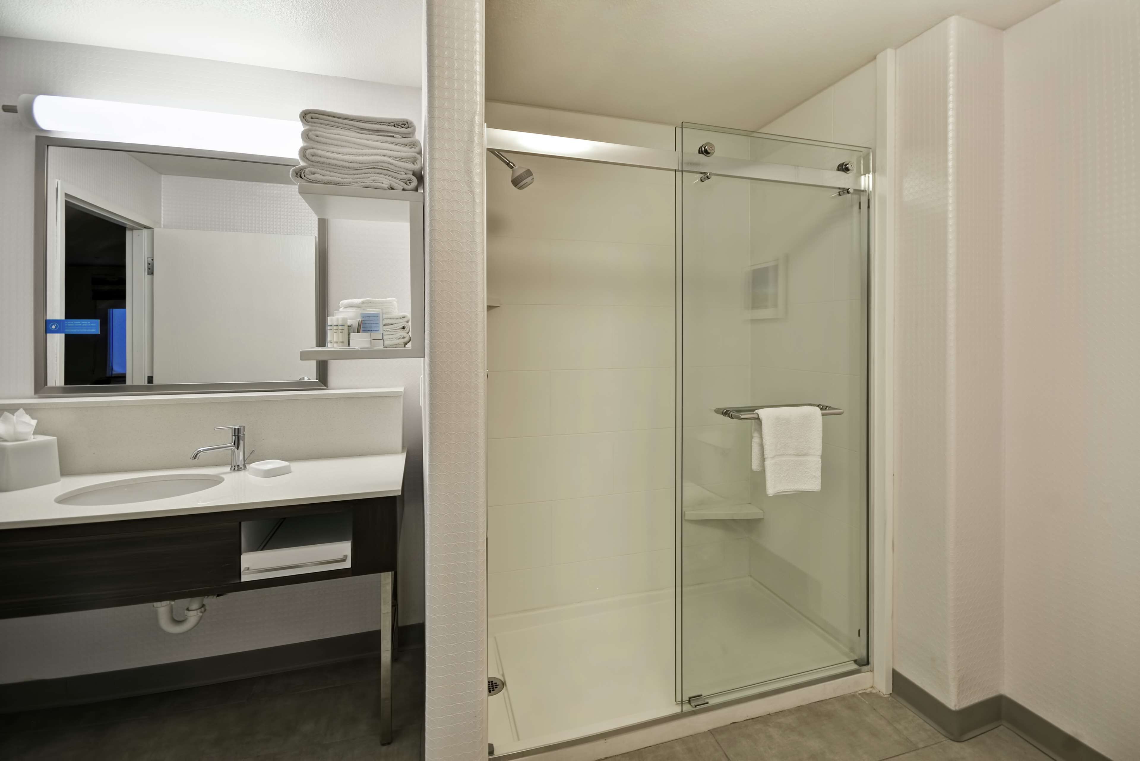 A modern bathroom with a glass-enclosed shower, a sink with a mirror, and neatly folded towels on a shelf.