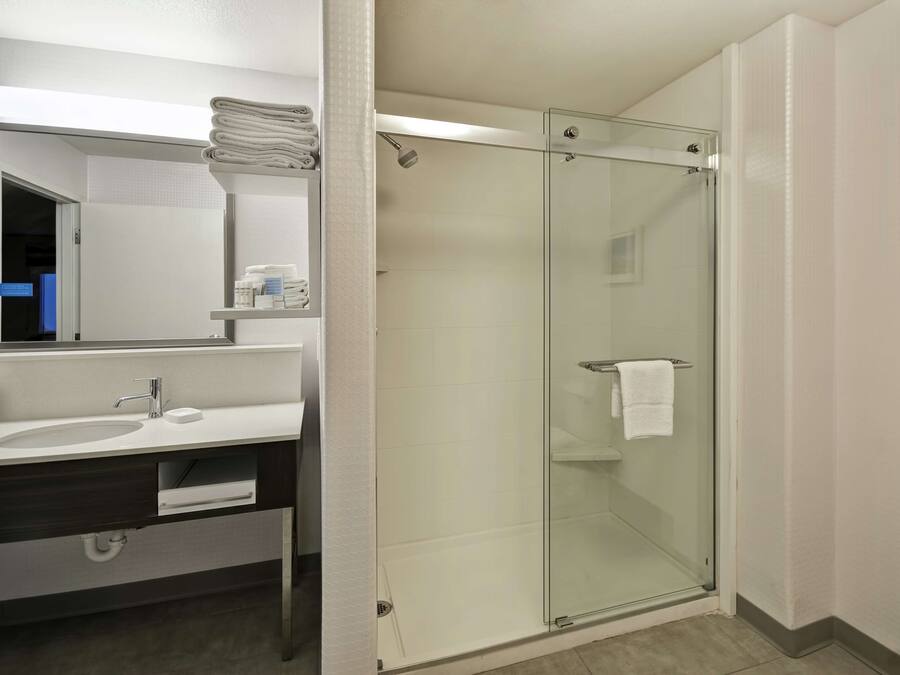 A modern bathroom with a glass-enclosed shower, a sink with a mirror, and neatly folded towels on a shelf.