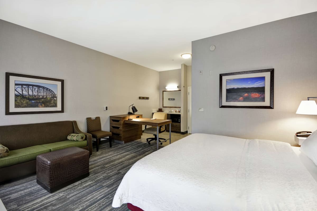 Ein Hotelzimmer mit einem Bett, einem Schreibtisch, einem Sessel, einer Couch und zwei gerahmten Bildern an den Wänden.