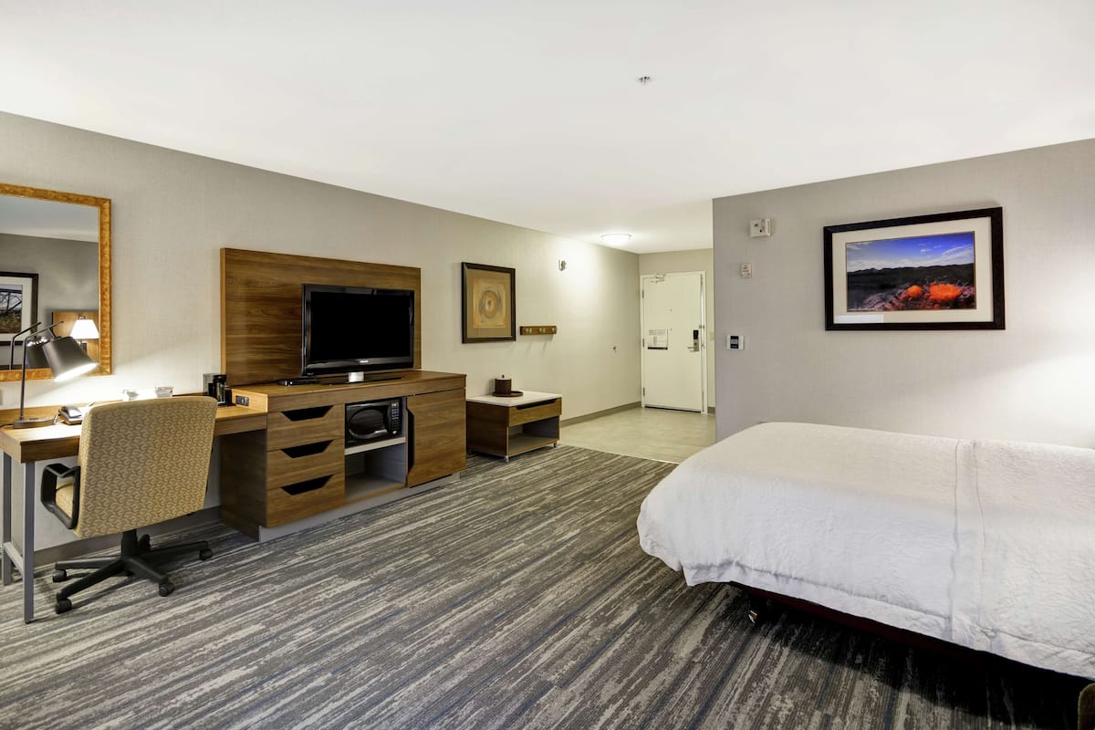 Ein Hotelzimmer mit Bett, Schreibtisch, Stuhl, Fernseher und einem gerahmten Bild an der Wand.