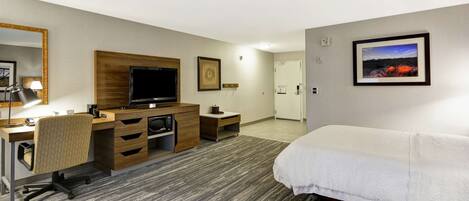 Habitación de hotel con cama, escritorio, silla, televisor y un cuadro en la pared.