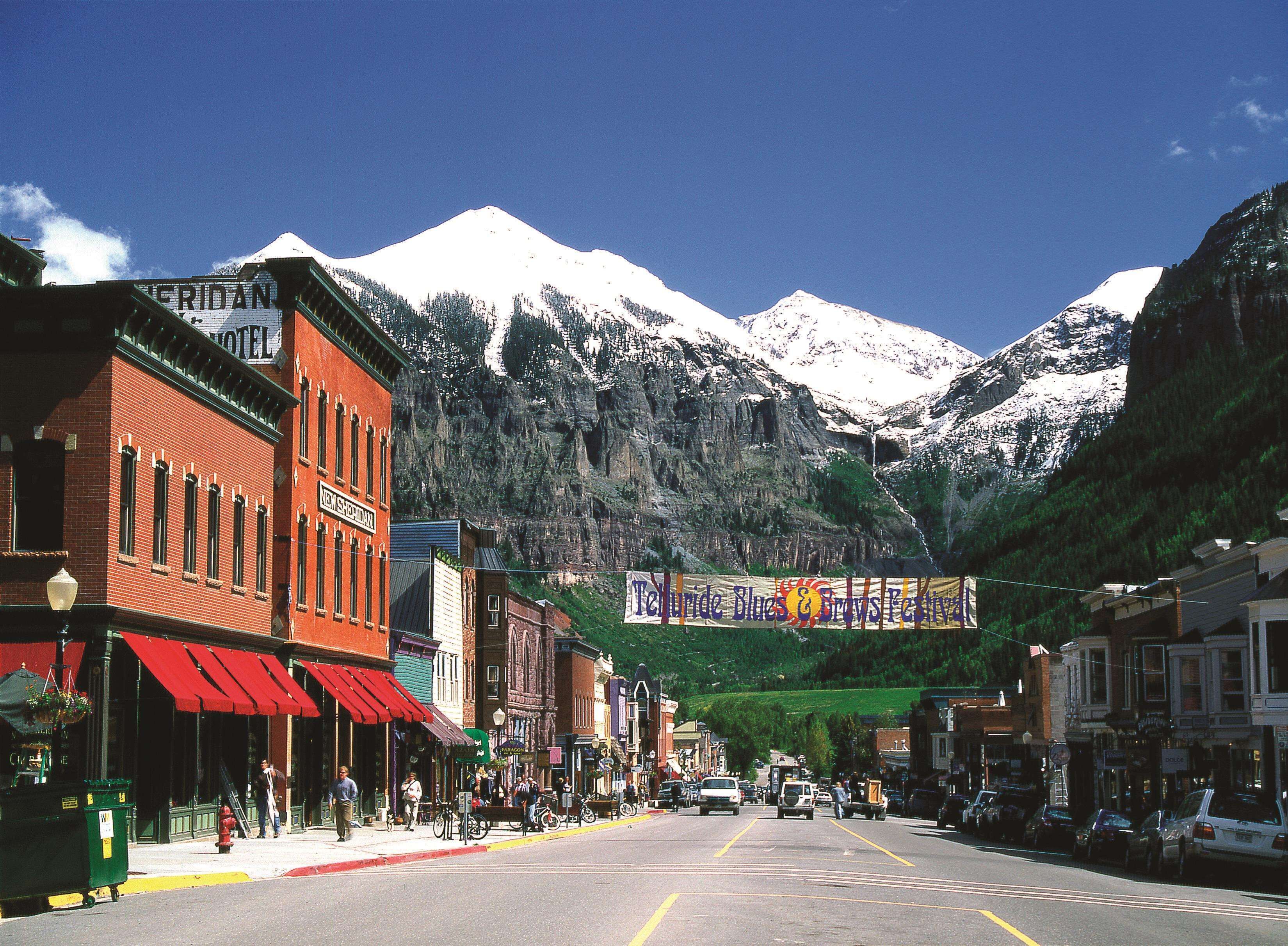 A street view with a hotel on the left, a banner for a music festival, and snow-capped mountains in the background.