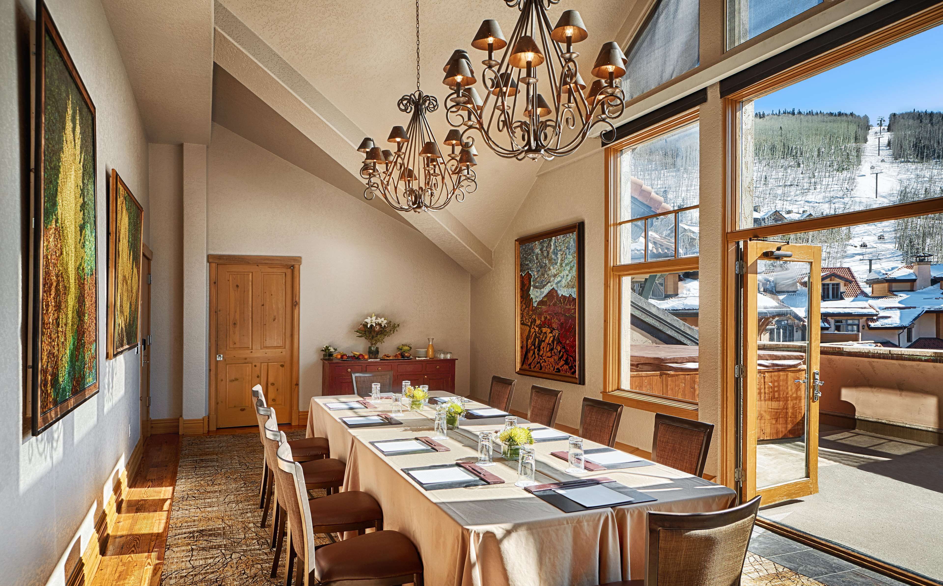 Comedor con una mesa larga dispuesta para seis comensales, una araña y ventanas amplias con vista a un paisaje nevado.