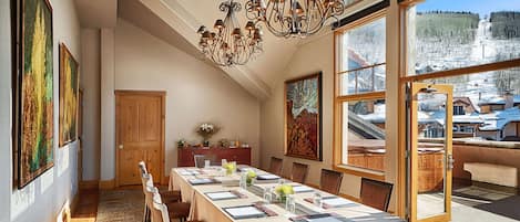 A dining area with a long table set for six, a chandelier, and large windows with a snowy landscape view.