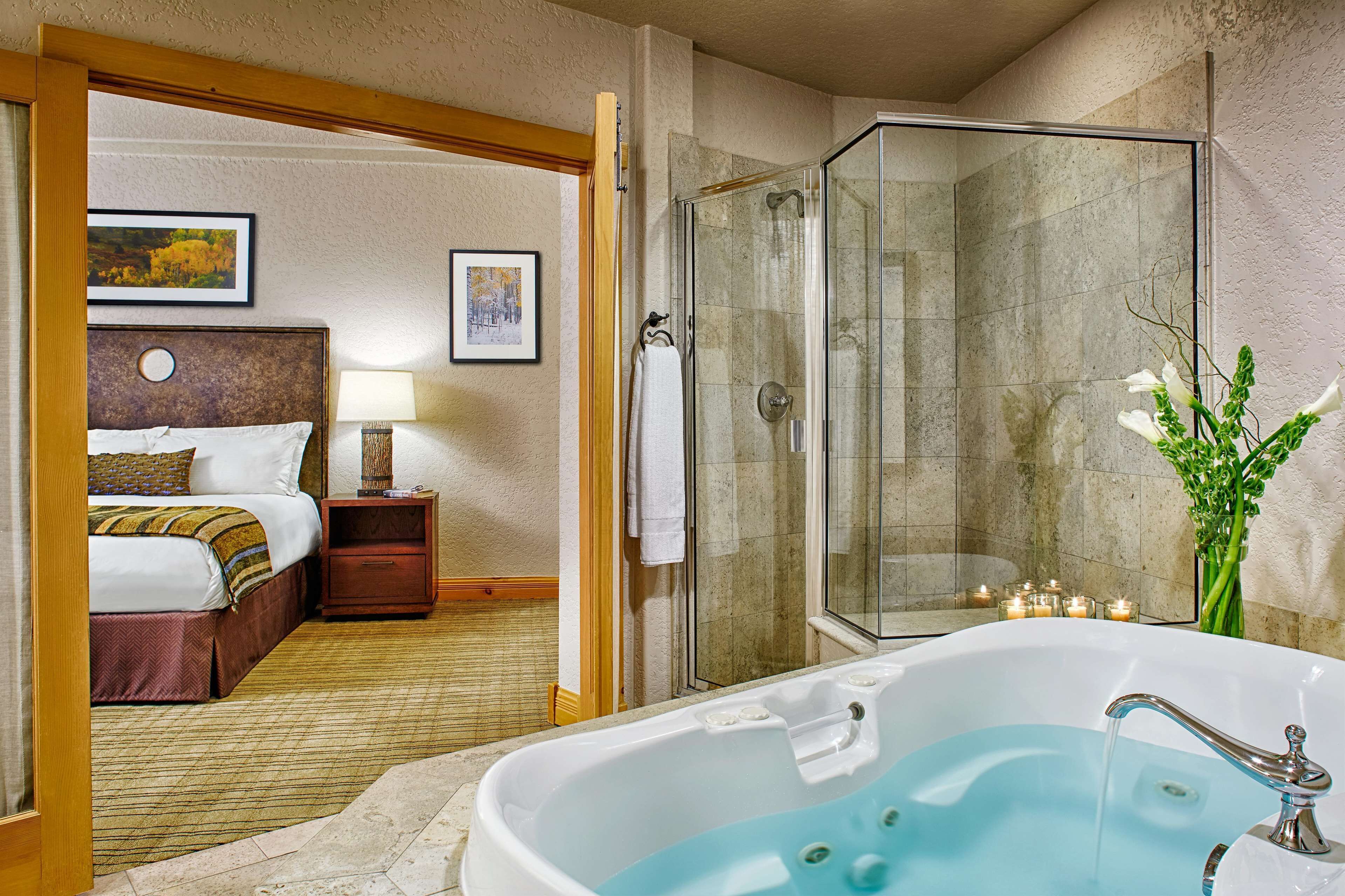 Une chambre d’hôtel avec une grande baignoire, une douche, un lit et une table de chevet avec une lampe.