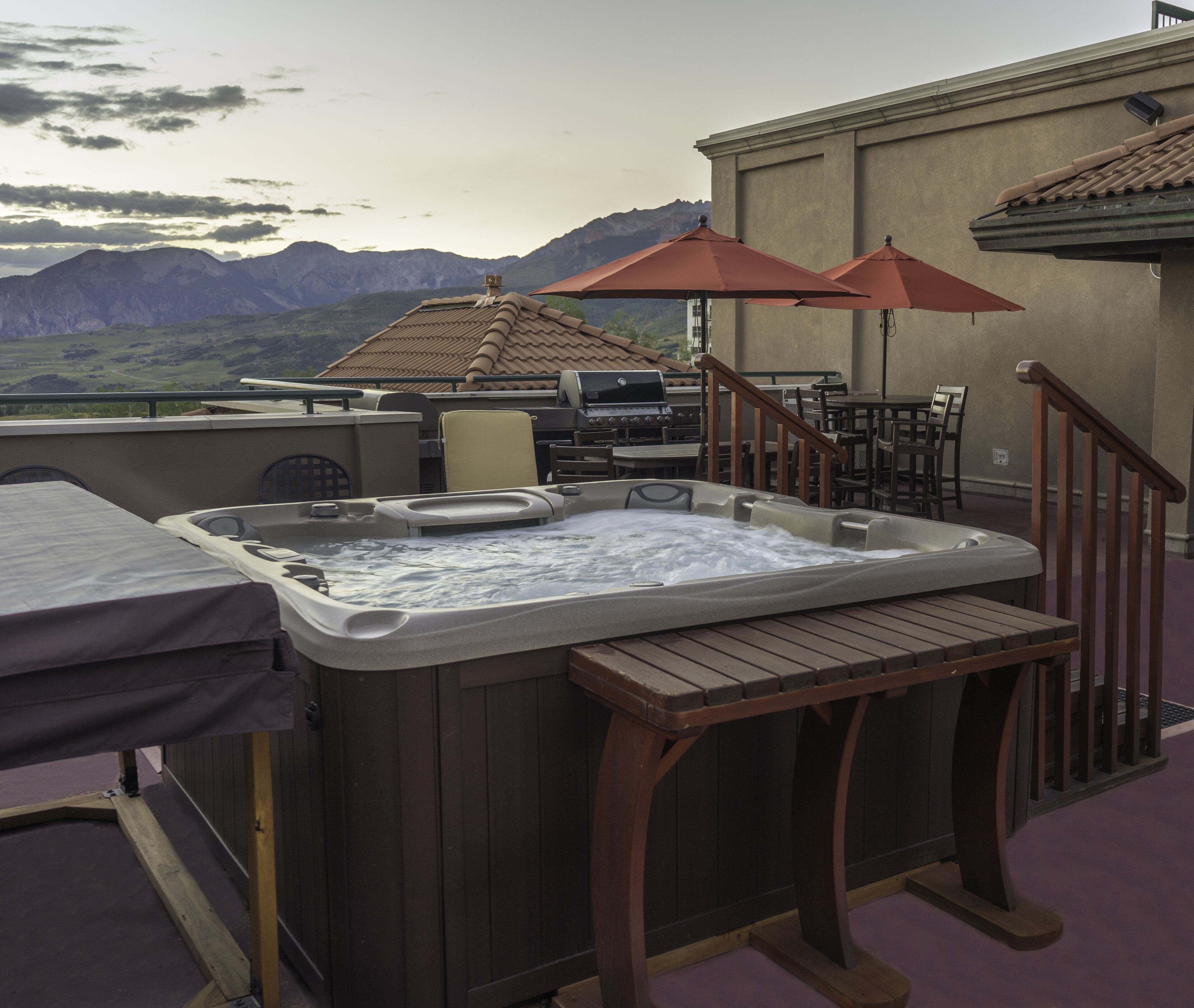 A hot tub on a patio with a mountain view, outdoor furniture, and a barbecue grill.