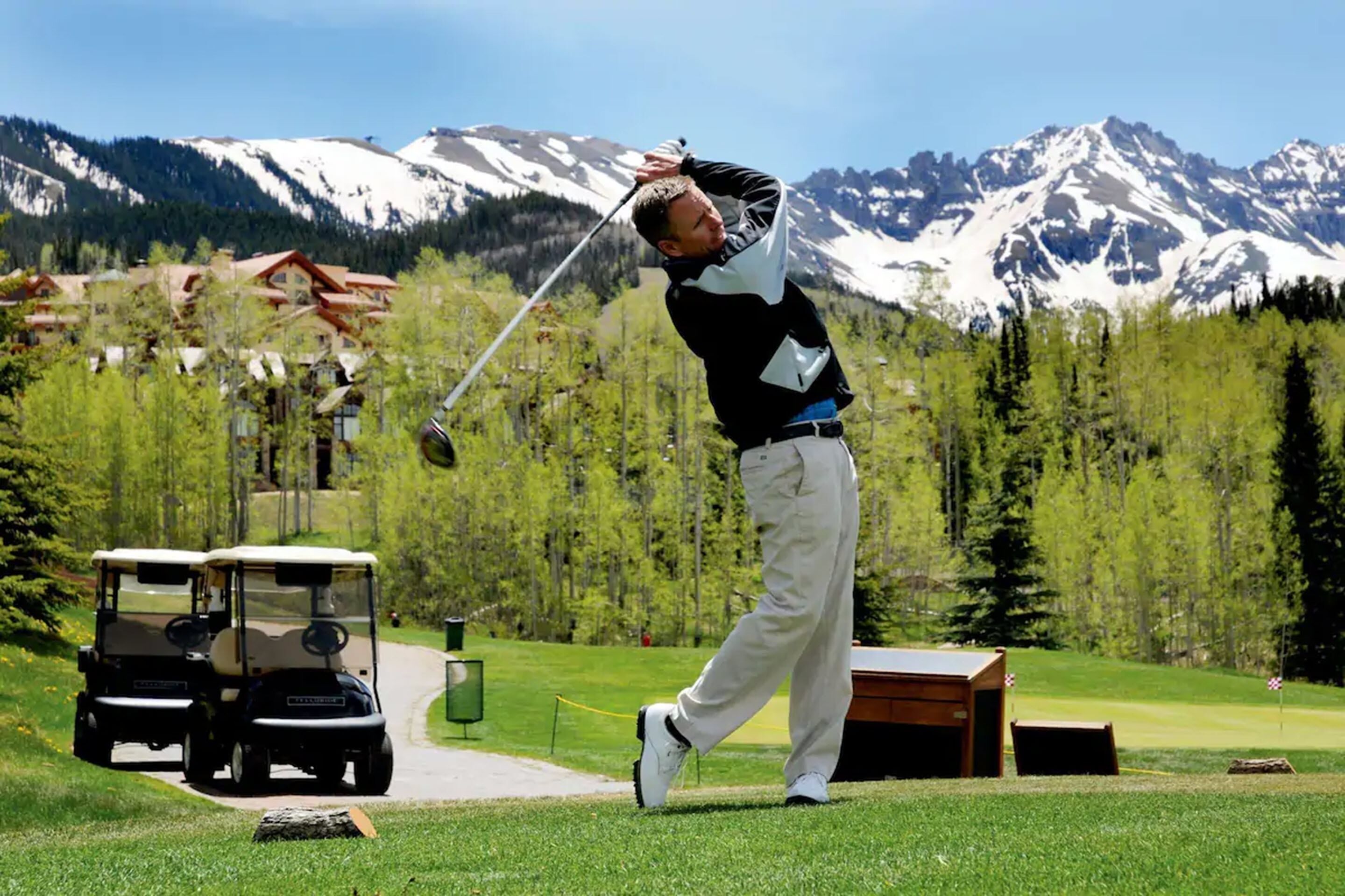 A golf course with a mountainous backdrop, a golf cart, and a wooden structure.