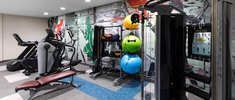 A gym with exercise equipment, a wall with a sports-themed mural, and a blue and gray carpet.
