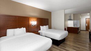 A hotel room with two beds, a wooden headboard, a wall-mounted light, a kitchenette, and a wooden floor. - Hawthorn Extended Stay by Wyndham College Station South (College Station)