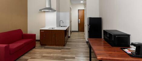 A compact kitchen with a wooden island, a red sofa, a microwave, and a coffee maker on a wooden table.